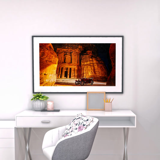 Framed artwork of a desert scene with architecture on a wall above a desk.