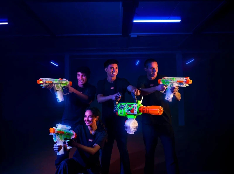 Group of people holding colorful laser tag guns in a dark room with blue lights.